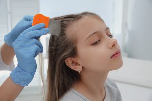 Professional lice technician using a metal nit comb on a young girl's hair under a bright work light inside a salon-style Montgomery County lice clinic, the literal scene a parent walks into when they book a first-time professional lice clinic visit.