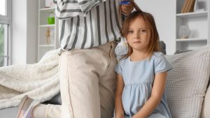 A mother carefully checking her young daughter's hair with a magnifying glass and a fine comb to identify whether a bug or speck is actually head lice, with the child sitting calmly on a sofa at home.