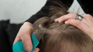A parent leaning in close under home lighting to check a child's hair part by part for head lice