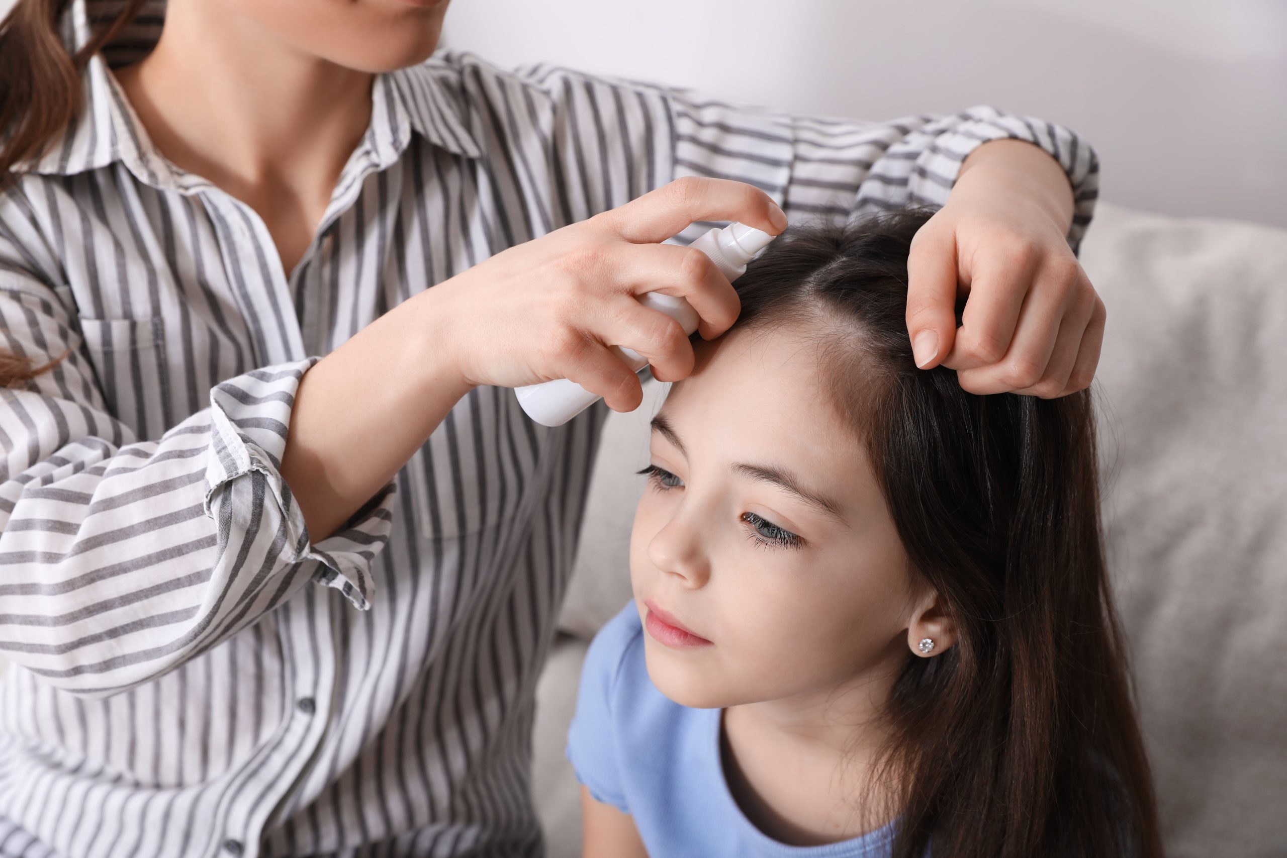 Parent applying an over-the-counter lice treatment to a child's hair at home, the moment before deciding whether to re-dose