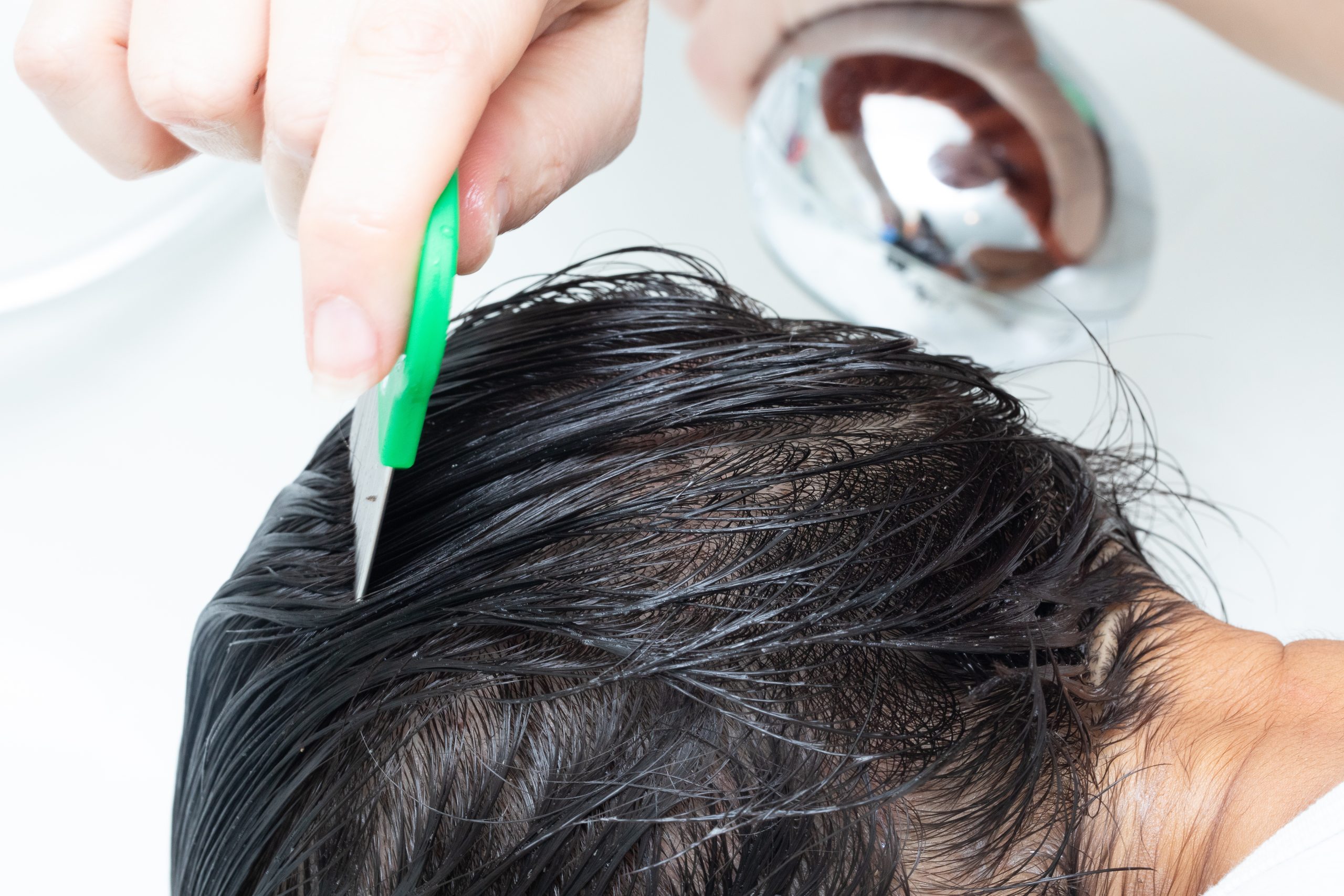Professional using a fine-toothed nit comb on a child's damp hair to remove lice and eggs