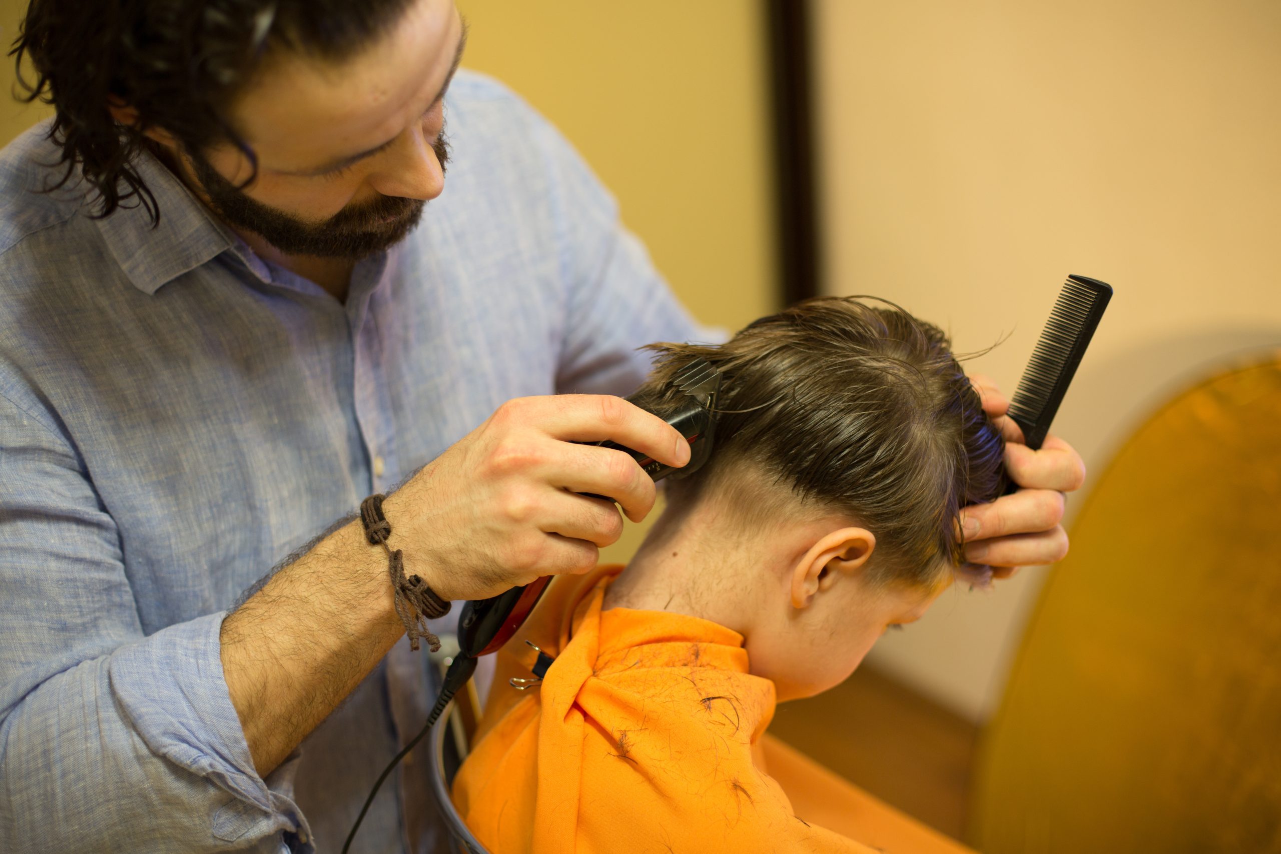 Child receiving a close haircut with clippers in a salon, illustrating the shaving-head lice question