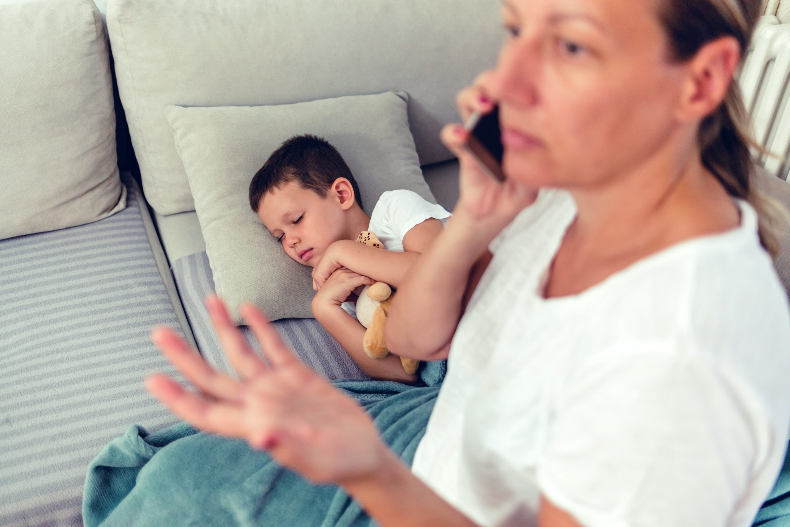 Worried parent on the phone while a child rests on the sofa, illustrating the emotional stress families can feel during a lice scare