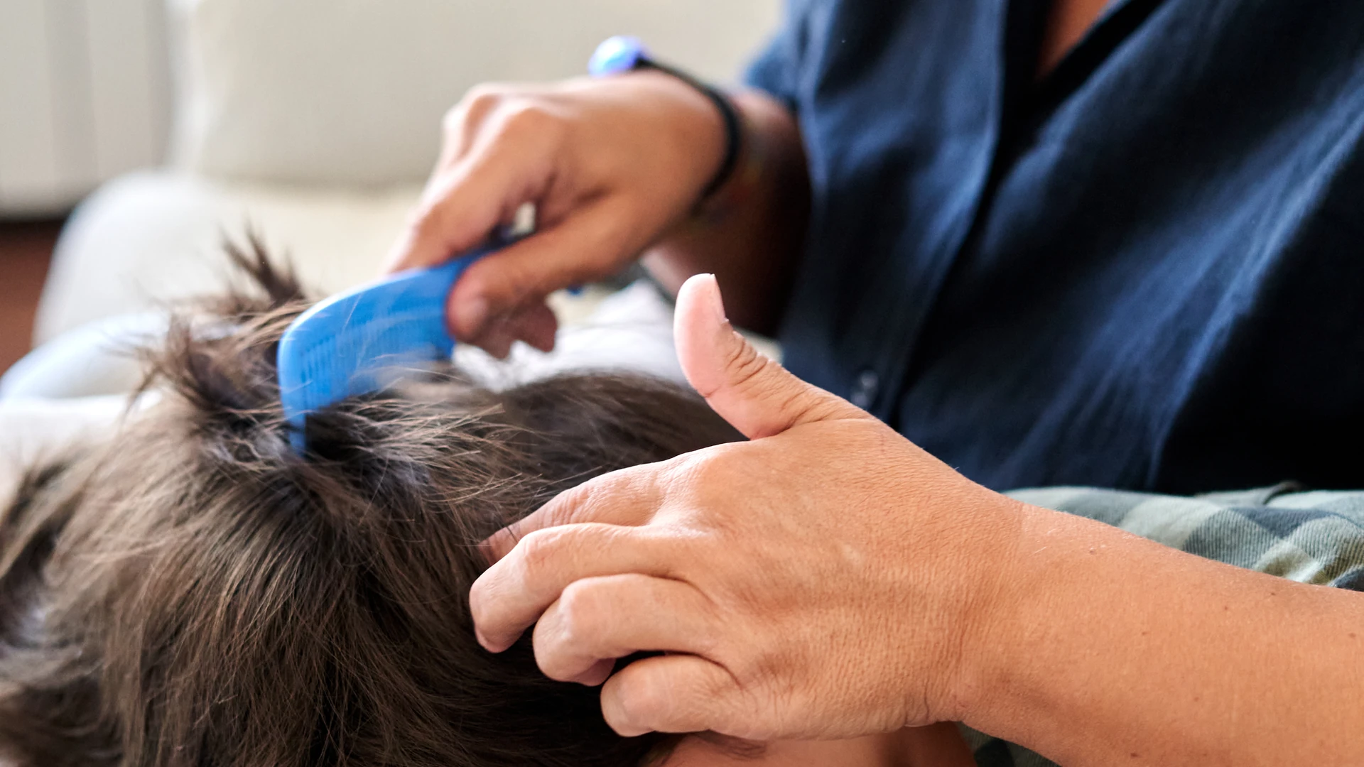 Hands combing dark brown hair with a blue comb while holding a section in place